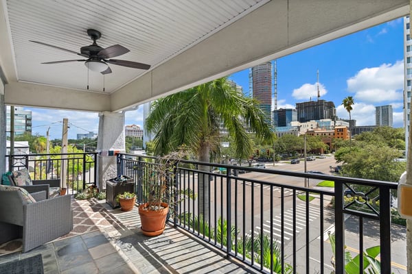 Covered balcony with ceiling fan overlooking downtown cityscape, palm tree, and street below